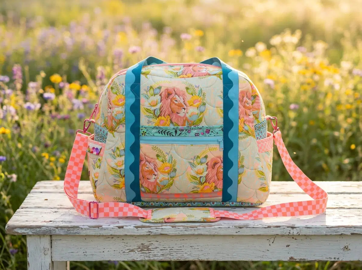 Custom handmade Ultimate Travel Bag 2.0 in floral fabric with colorful straps, photographed in a wildflower garden