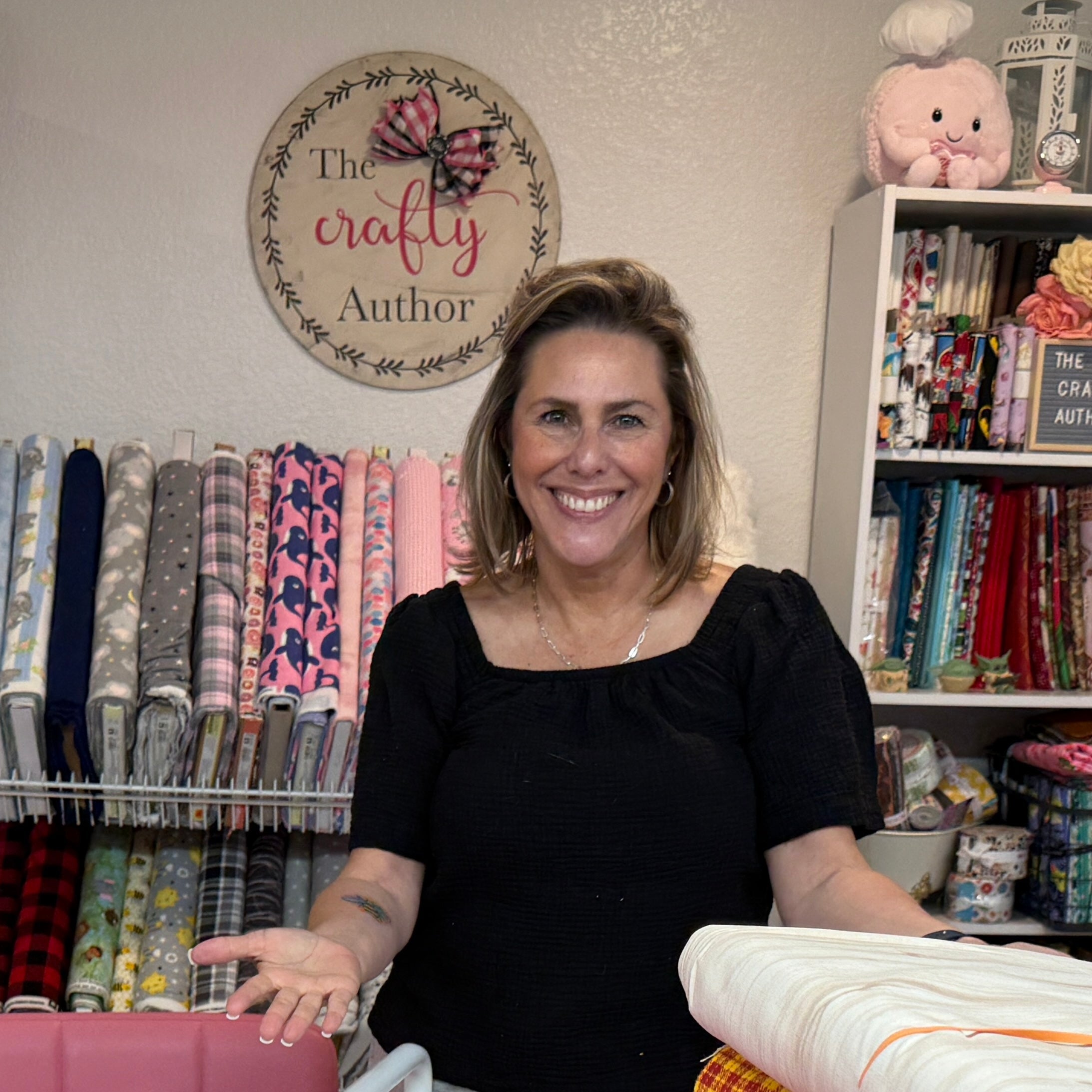 Woman standing behind a table with fabric rolls in a store setting.